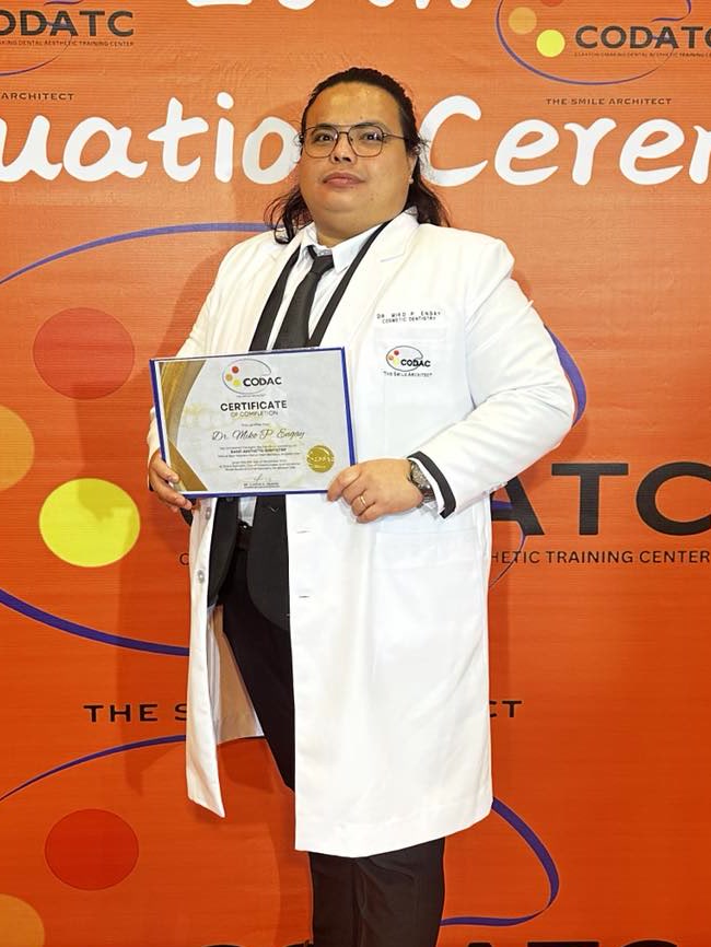 Dr. Miko P. Engay in a white coat, holding a certificate of completion from a dental aesthetic training course